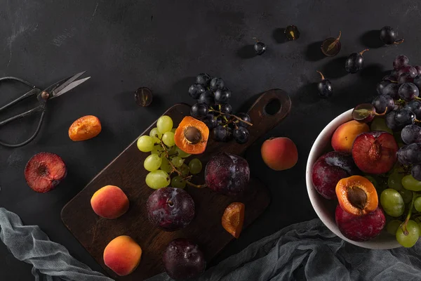 Fruits Still life with fruit on whte ceramic bowl. Concrete wall. Dramatic light. Grapes, apricots and plums.