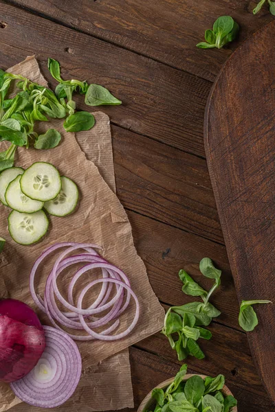 Top uitzicht van houten snijplank op oude houten tafelblad met tafelkleed, gesneden rode ui en komkommer en maïs salade — Stockfoto