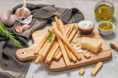 Geleneksel İtalyan ekmeği Grissini biberiye, parmesan peyniri, zeytinyağı, sarımsak ve tuz ile gri arka planda..