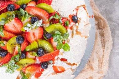 Kremalı Pavlova pastası ve taze yaz meyveleri ve ahşap arka planda kivi. Pavlova tatlısını orman meyvesi ve nane ile kapat. Yemek fotoğrafçılığı