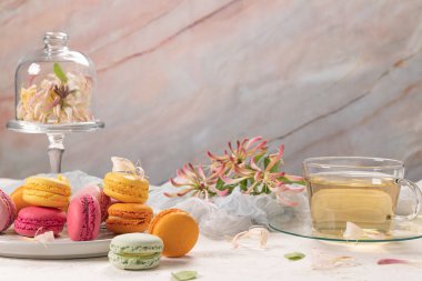 Renkli Fransız kurabiyeleri. Yasemin çiçekli kurabiyeler ve beyaz masa arkasında çay. Seçici odak