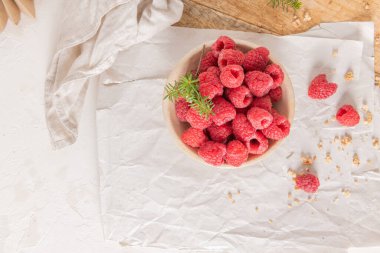 Taze ahududu ve ahşap tepside dağınık tahıl gevreğiyle dolu kırsal seramik bir kasenin yukarıdan çekimi.