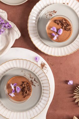 Mor çiçekler ve çikolata talaşlarıyla süslenmiş, kumaşla kaplanmış iki kremalı çikolatalı mus manzarası..