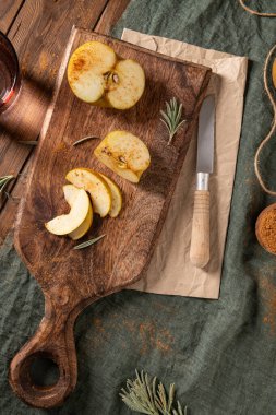 Dilimlenmiş bir Reinette elmasının düzlüğü tarçınlı, tahta bir tahtada, bıçaklı ve biberiyeli..