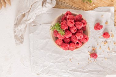 Taze ahududu ve ahşap tepside dağınık tahıl gevreğiyle dolu kırsal seramik bir kasenin yukarıdan çekimi.
