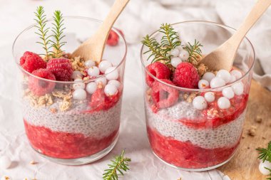 İki bardak katmanlı ahududu ve taze ahududu ve beyaz yaban mersinli chia tohumu pudingi.