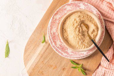 Yakın çekim, yukarıdan aşağıya bir kâse kahverengi şeker kaşık, ahşap tahta tahta, taze stevia yaprakları ve pembe bir peçete.