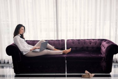 Ev ofis. Oturma odasında kanepede oturan ve dizüstü bilgisayar kullanarak başarılı genç güzel kadın.