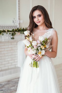 Sıska, güzel bir kadın panoramik pencerenin yanında lüks gelinlik giyiyor. Çiçekleri tutan muhteşem gelin.