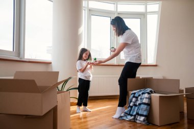 Oturma odasında oturan mutlu, tatlı anaokulu kızı. Yeni daireye taşınacağı için heyecanlı. Kutuda gülümseyen genç annesiyle.