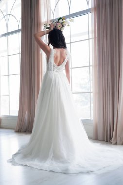 Kıvırcık saç modeli ve yatak odasında pencere yakınında duran uzun peçe ile beyaz ipek sabahlık güzel gelin portresi, kopya alanı. Gelinler sabah hazırlığı. Geri görünüm