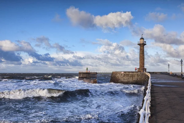 Wind and a rising tide produce rough seas at the entrance to Whitby Harbour in North Yorkshire, on a bright winter afternoon.