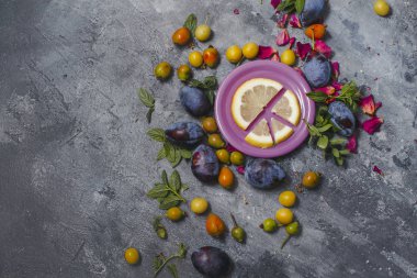 dilimlenmiş limon ve gri arka plan üzerinde dağınık bir renkli meyveleri pembe bir tabak