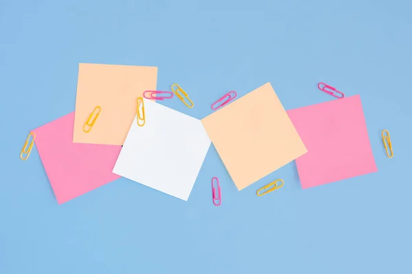 Square colored sticky notes and paper clips on a blue background.