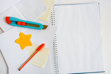 Kafeste büyük açık bir defter, birkaç not defteri yıldız şeklinde yapışkan bir not, kırtasiye bıçağı ve beyaz arka planda bir kalem. Metin için alanı olan düz bir düzen
