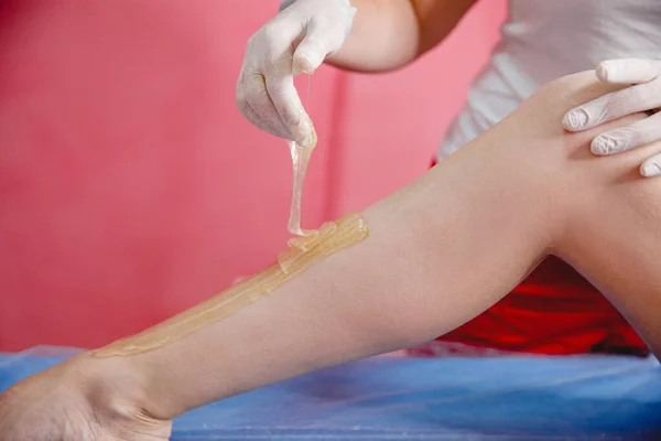 the master of sugaring in gloves puts paste on the clients leg in the salon. The procedure of sugar hair removal