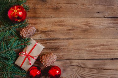 Köknar dalları, el işi hediyeleri, koniler ve ahşap bir arka planda kırmızı takılar. Metin için yer