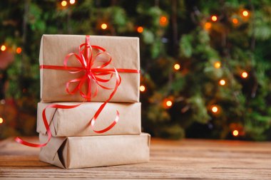 Ahşap bir masanın üzerinde kırmızı kurdeleli el sanatları kağıdının içinde renkli bir bokeh 'in arka planına karşı bir yığın Noel hediyesi. Yüksek kalite fotoğraf