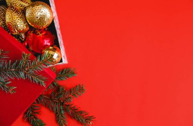 Kırmızı arka planda kırmızı ve altın renkli Noel topları olan hediye kutusunu aç. Ladin dalının yanında. Yüksek kalite fotoğraf