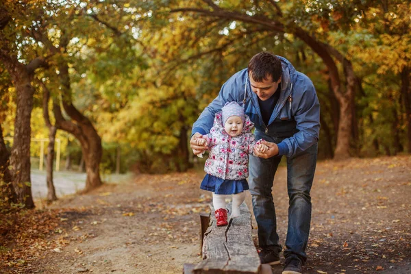 Young dad teaches his little daughter to walk in the Park in the fall