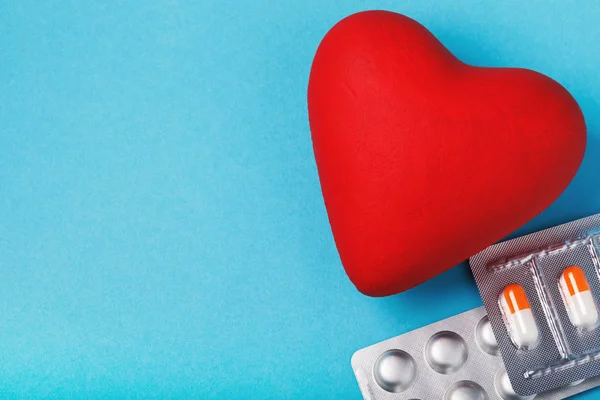 An object in the shape of a heart and pills on a blue table with copy space.