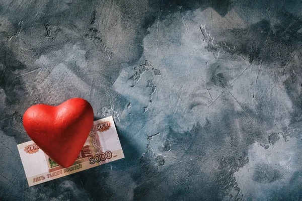 Love for money. Red heart and five thousand rubles on the table with copy space, top view of the overall plan