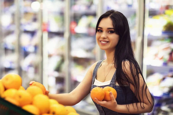 A customer in a mall chooses oranges. The girl in the store hold