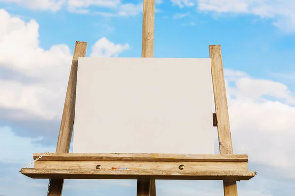 Blank white canvas on an easel against the background of the sky with clouds