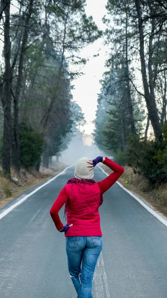 Rear view of a woman dressed in winter in the middle of a lonely road in a forest