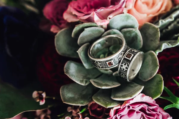 Close-up of vintage wedding rings on floral bouquet with succulent plant and roses