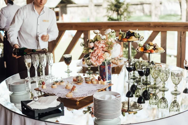 Waiter pouring wine in glasses on served table for wedding banquet