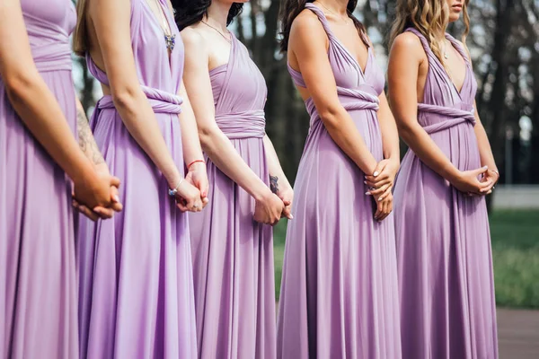 Cropped view of bridesmaids in lilac dresses standing outdoors