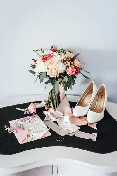 Wedding arrangement of rings, invitation letter, bouquet and stylish shoes