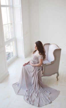 Hamile bir kadın uzun saçlı ve güzel bir uzun elbiseli bir sandalyeye oturur. Tren ile uzun elbise