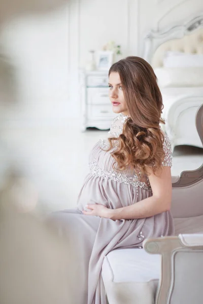 Uma mulher grávida com cabelos longos e em um belo vestido longo senta-se em uma cadeira — Fotografia de Stock