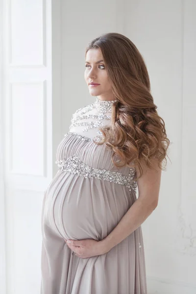 Uma mulher grávida com cabelos longos e em um belo vestido longo. Abraços grávidas barriga — Fotografia de Stock