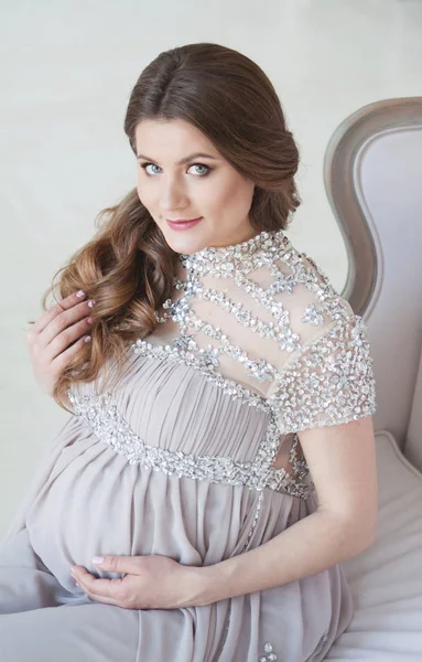 임신한 여자 긴 머리와 아름 다운 긴 드레스를 입고의 자에 앉아서 카메라에서 보이는 — 스톡 사진