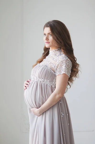 Uma mulher grávida com cabelos longos e em um belo vestido longo. Abraços grávidas barriga — Fotografia de Stock