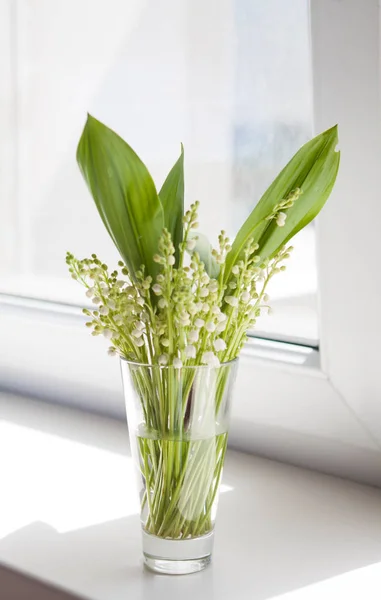 Un ramo de flores blancas de lirios del valle con hojas verdes de pie en un vaso en el alféizar de la ventana Fotos De Stock Sin Royalties Gratis