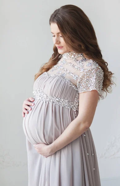 Kobieta w ciąży, z długimi włosami i w pięknej długiej sukni. Brzuch w ciąży uściski — Zdjęcie stockowe