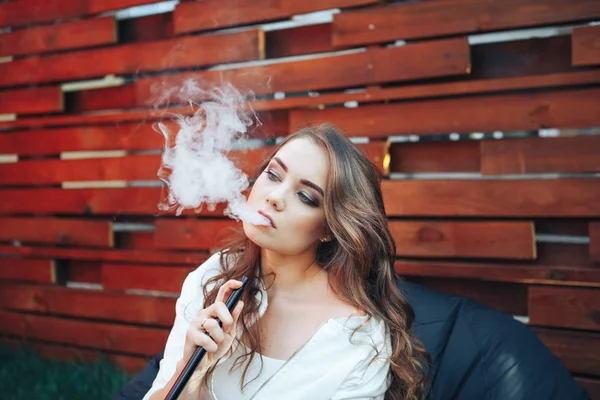 Young woman smoking a hookah outdoors. The pleasure of smoking. Portrait of a smoking young woman. Background a wooden wall — Stock Photo, Image