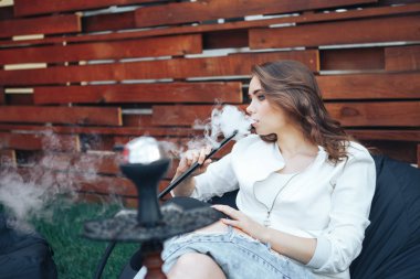 Genç kadın bir nargile açık havada sigara. Sigara zevk. Arka plan bir ahşap duvar