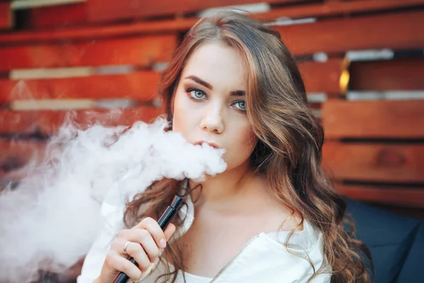 Young woman smoking a hookah outdoors. The pleasure of smoking. Portrait of a smoking young woman. Background a wooden wall