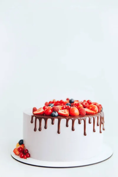 Pastel con crema de queso blanco, decorado con ganache y bayas rojas en un soporte blanco Fotos De Stock