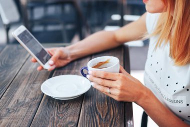 Cep telefonu ve bir fincan kahve tutan kadınların elleri yakın çekim