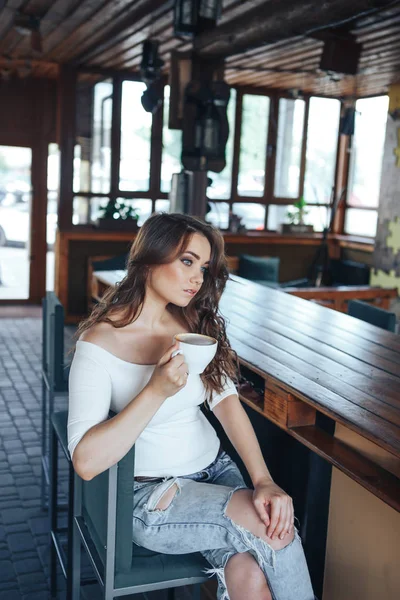 Young woman sits on a chair at a bar counter and drinks coffee — Stock Photo, Image