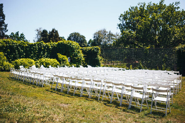 White chairs stand in the rows on green lawn