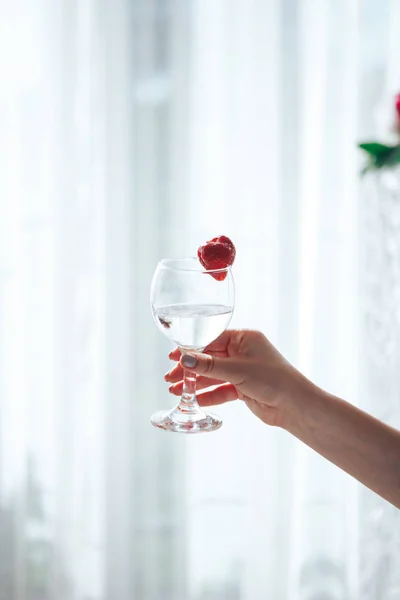 Mano femminile che tiene un bicchiere di vino con le fragole fuori dalla finestra — Foto Stock