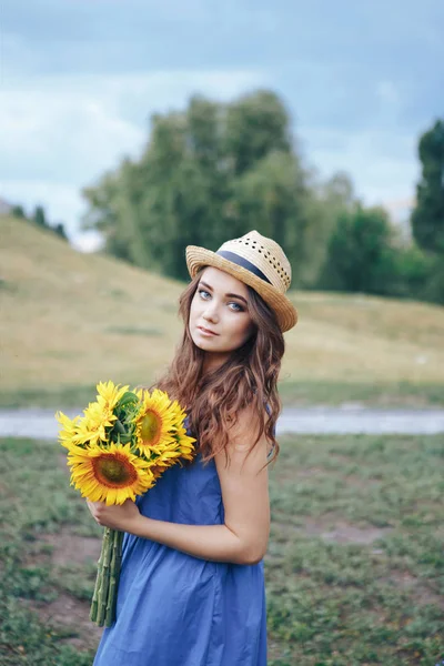 Ayçiçeği ile bir parkta hasır şapkalı bir genç kadın
