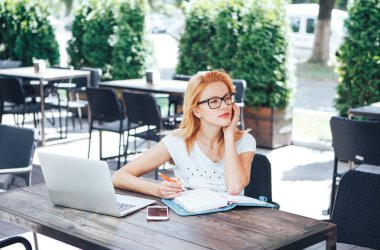 Kızıl saçlı kadın ne bir defter bir yaz kafede yazmak düşünüyor. Genç bir kadın oturuyor bir kafe ve işleri.